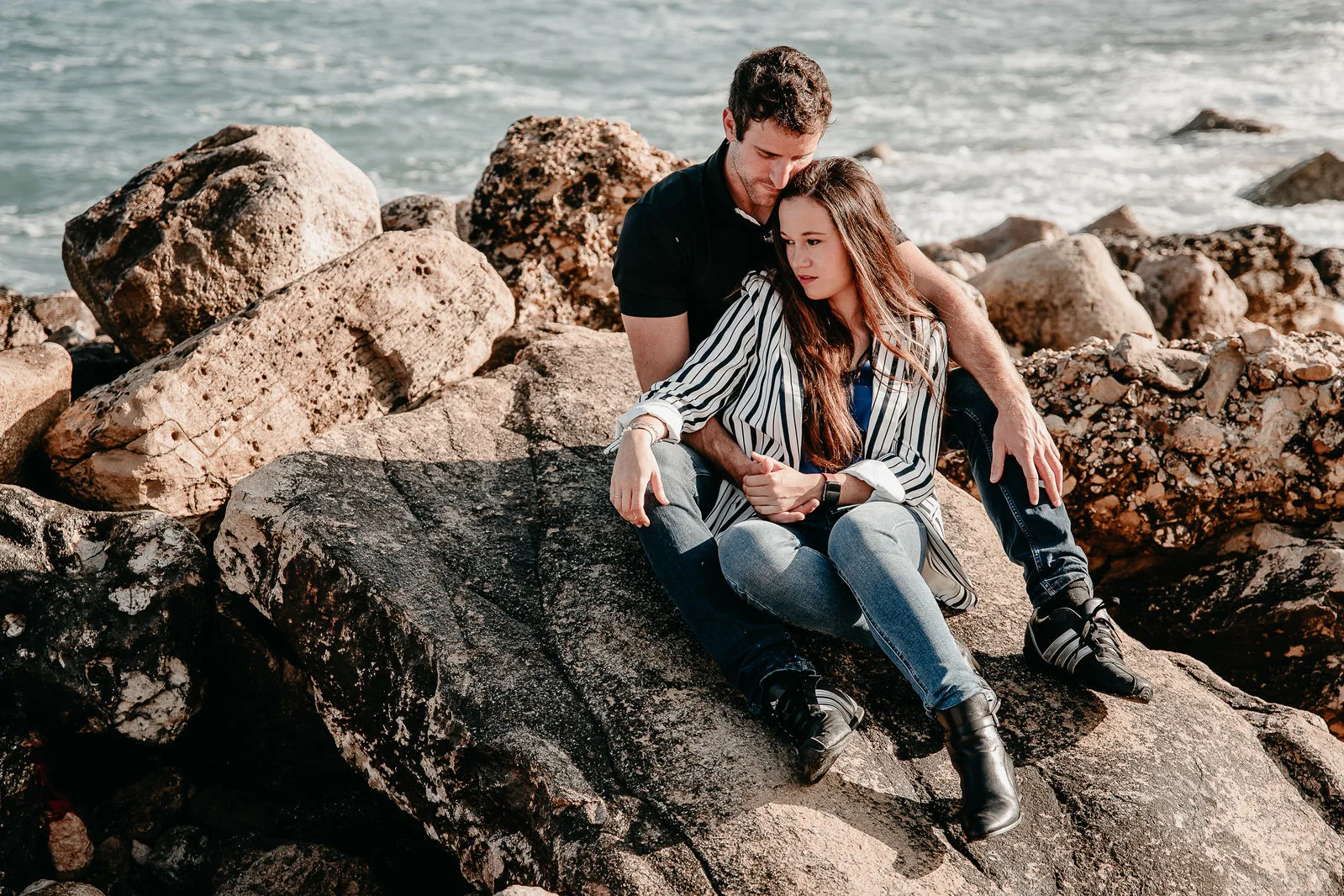Pareja sentada entre las rocas junto al mar