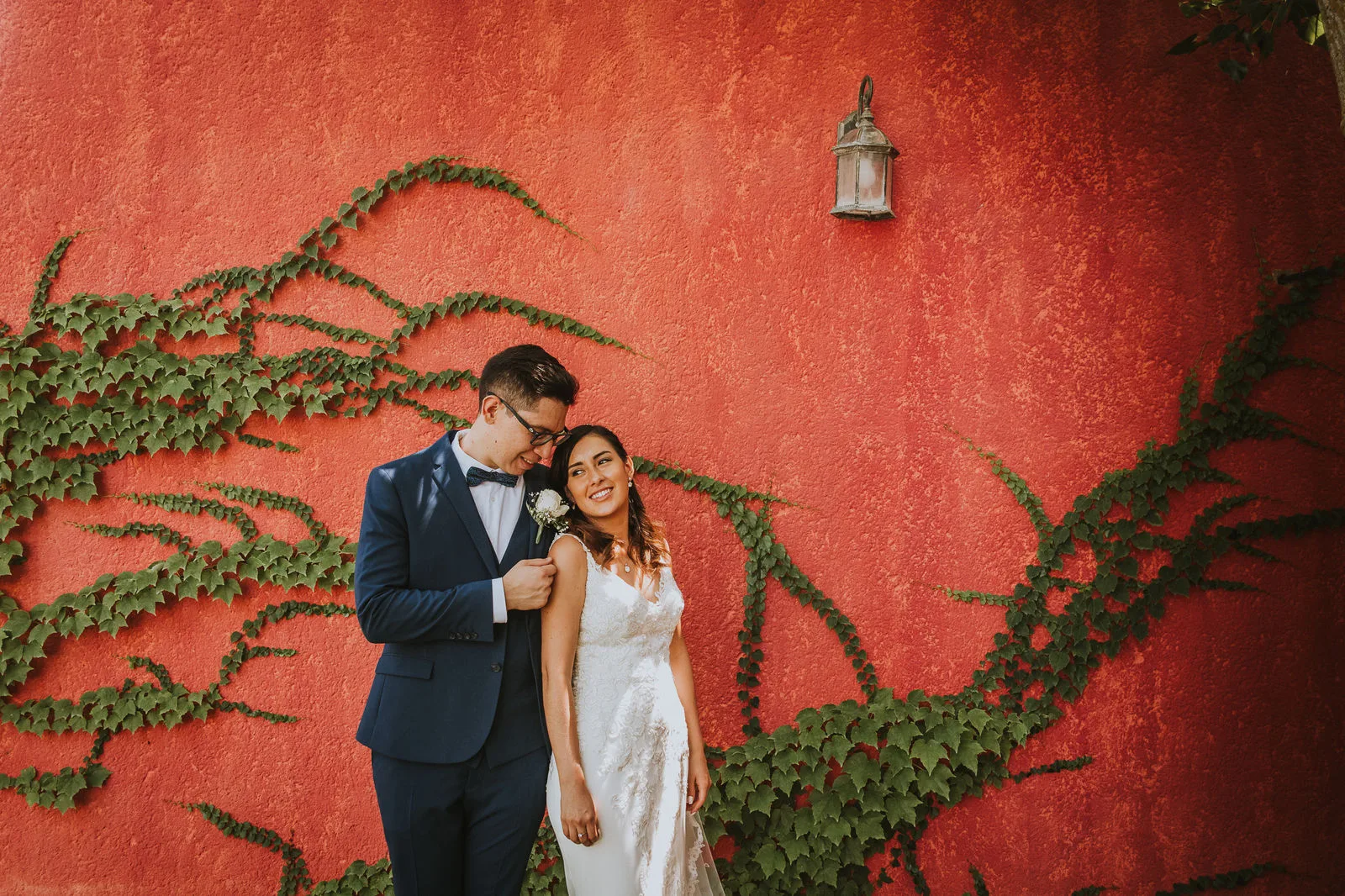 Pareja frente a un muro rojo cubierto de hiedra